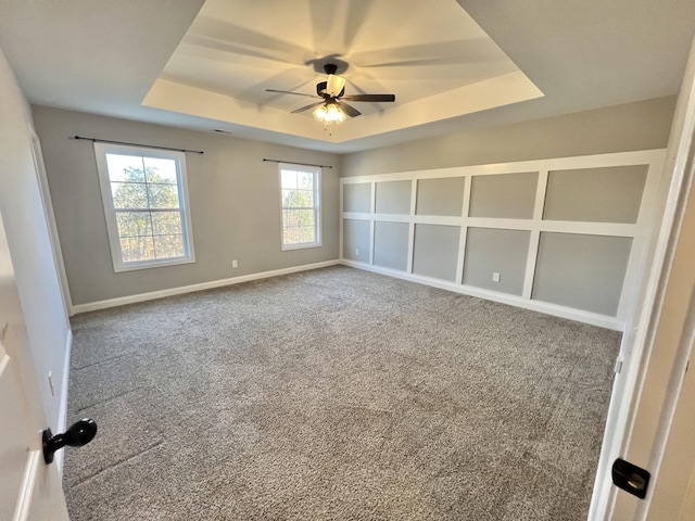 carpeted empty room featuring a tray ceiling, a ceiling fan, and baseboards