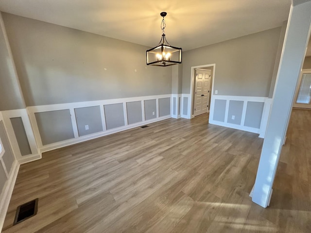 unfurnished dining area with visible vents, a decorative wall, a notable chandelier, and wood finished floors