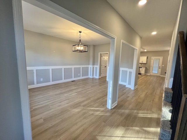 unfurnished dining area featuring a wainscoted wall, an inviting chandelier, light wood-type flooring, a decorative wall, and recessed lighting