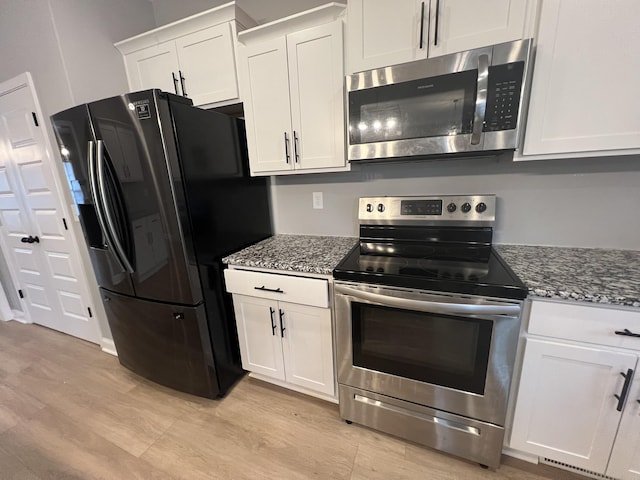 kitchen with light wood-style floors, white cabinetry, stainless steel appliances, and dark stone countertops