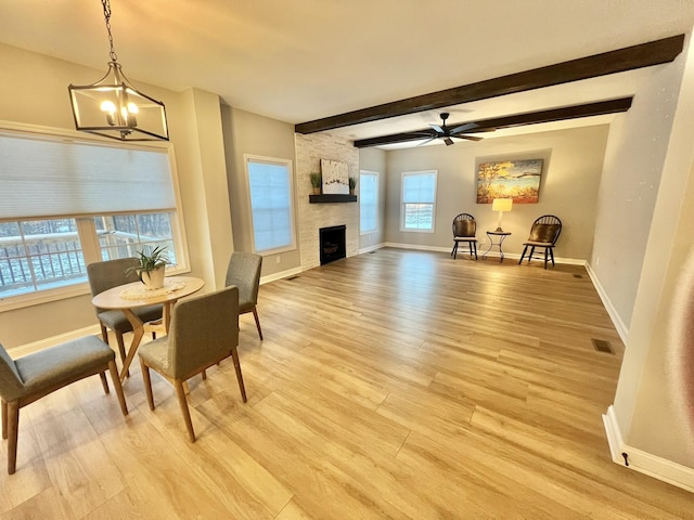 dining area with baseboards, light wood-style floors, a fireplace, beam ceiling, and ceiling fan with notable chandelier