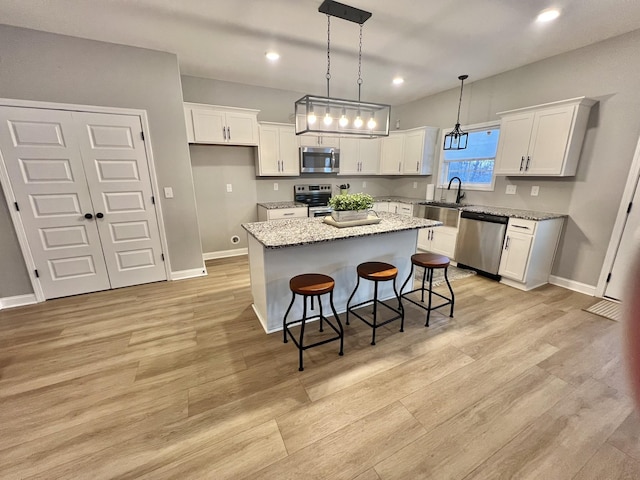 kitchen featuring pendant lighting, appliances with stainless steel finishes, white cabinetry, a kitchen island, and light stone countertops