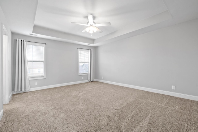 carpeted empty room with a raised ceiling, a healthy amount of sunlight, and ceiling fan