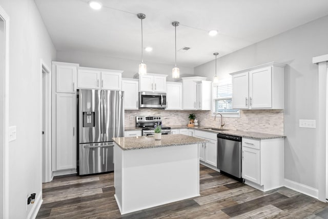 kitchen with pendant lighting, appliances with stainless steel finishes, a center island, white cabinetry, and light stone counters