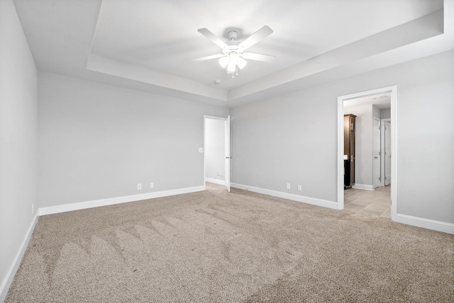 unfurnished room with a raised ceiling, light colored carpet, and ceiling fan