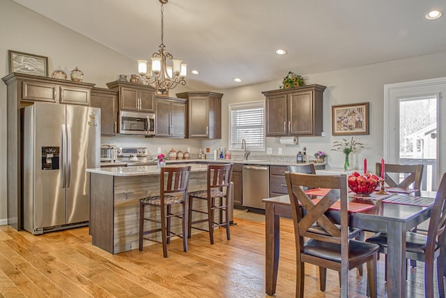 kitchen with decorative light fixtures, vaulted ceiling, a kitchen island, light wood-type flooring, and appliances with stainless steel finishes