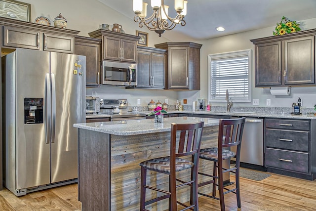 kitchen with light stone countertops, dark brown cabinetry, decorative light fixtures, stainless steel appliances, and light hardwood / wood-style flooring