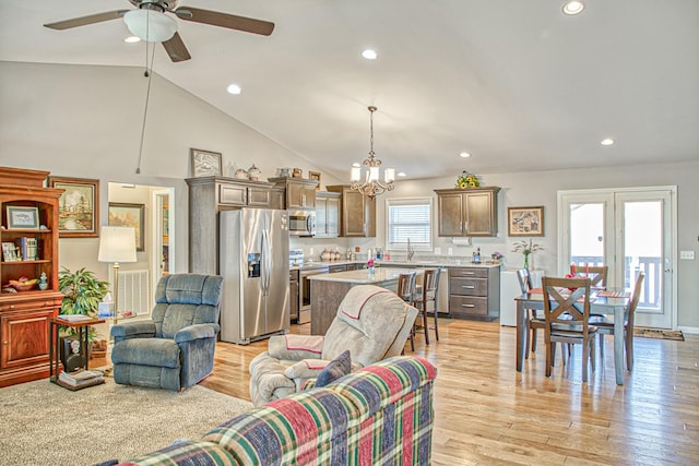 living room featuring ceiling fan with notable chandelier, light wood-type flooring, high vaulted ceiling, and a healthy amount of sunlight