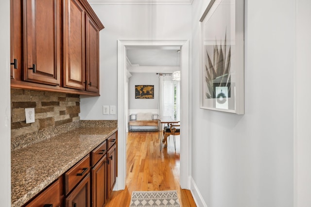 kitchen featuring light wood-type flooring, ornamental molding, stone countertops, and tasteful backsplash