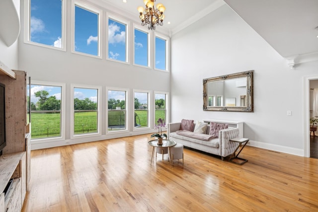 living room with a wealth of natural light, ornamental molding, a towering ceiling, and an inviting chandelier