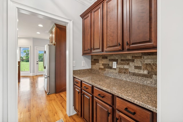 kitchen featuring stainless steel fridge, backsplash, light wood-type flooring, dark stone countertops, and ornamental molding