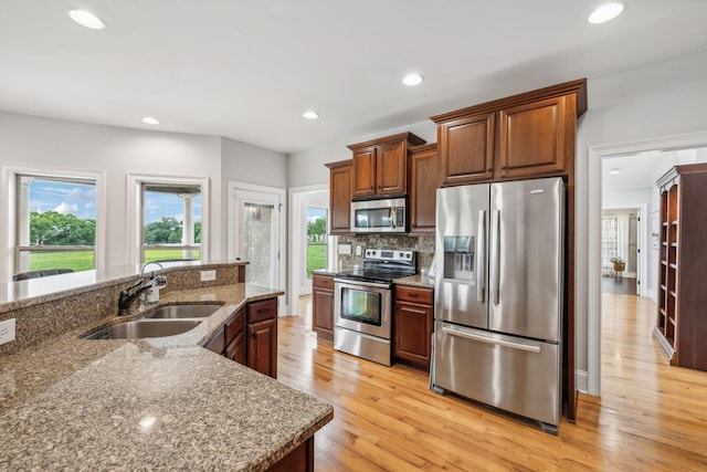 kitchen featuring light hardwood / wood-style floors, appliances with stainless steel finishes, backsplash, light stone counters, and sink