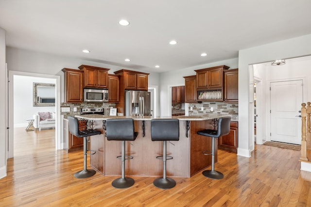 kitchen with a kitchen bar, backsplash, appliances with stainless steel finishes, and a center island with sink