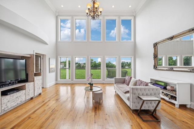 living room featuring a chandelier, crown molding, a towering ceiling, and light hardwood / wood-style flooring