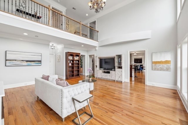 living room with wood-type flooring, a high ceiling, a chandelier, and ornamental molding