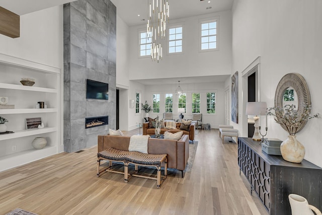 living room featuring a notable chandelier, light wood-type flooring, a fireplace, built in features, and a towering ceiling