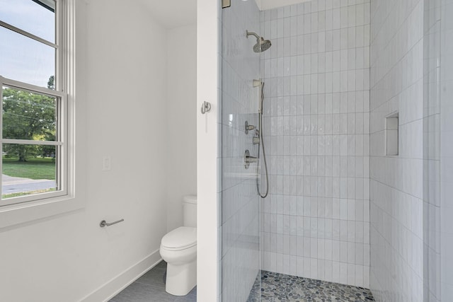 bathroom with toilet, tile patterned flooring, a wealth of natural light, and tiled shower