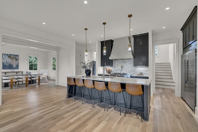 kitchen with an island with sink, pendant lighting, high end refrigerator, and custom range hood