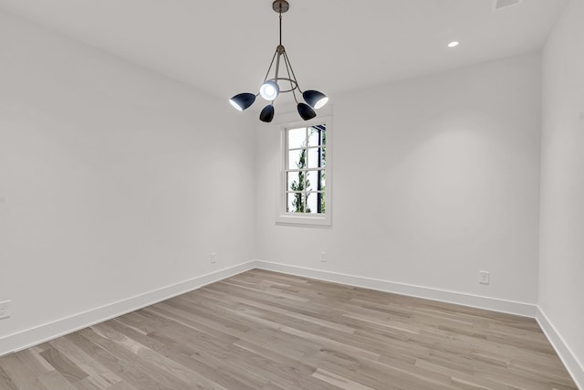 spare room with a chandelier and light wood-type flooring