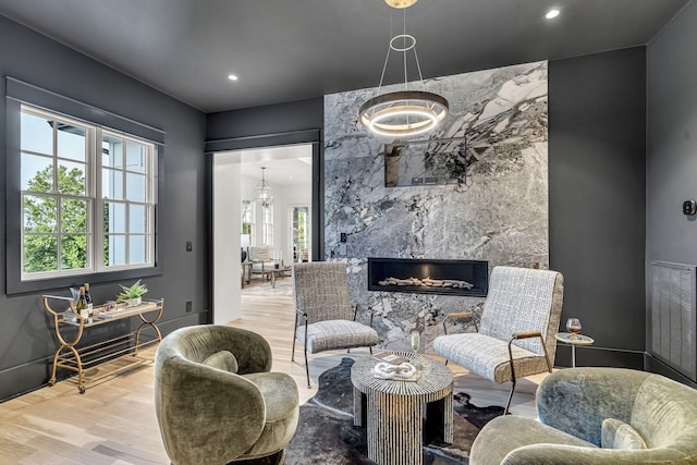 living area featuring light wood-type flooring, a high end fireplace, a wealth of natural light, and a notable chandelier