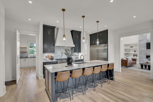 kitchen featuring built in fridge, decorative backsplash, hanging light fixtures, a breakfast bar, and custom range hood