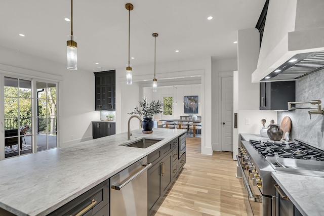 kitchen with light hardwood / wood-style floors, stainless steel appliances, pendant lighting, wall chimney exhaust hood, and sink