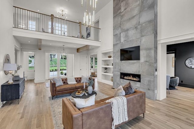 living room featuring a high ceiling, light hardwood / wood-style flooring, built in features, and a fireplace