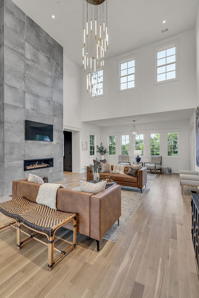 living room with a high ceiling, light hardwood / wood-style flooring, a chandelier, and a fireplace