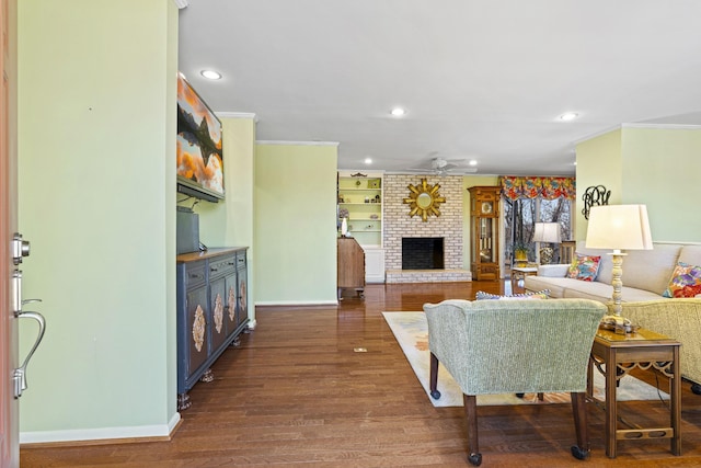 living room featuring ceiling fan, a brick fireplace, dark wood-type flooring, ornamental molding, and built in shelves