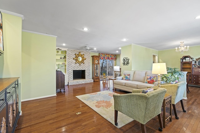 living room with a fireplace, dark hardwood / wood-style floors, built in features, ornamental molding, and ceiling fan with notable chandelier