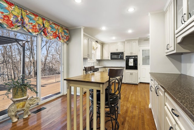 kitchen with black appliances, white cabinetry, dark stone countertops, backsplash, and dark hardwood / wood-style floors