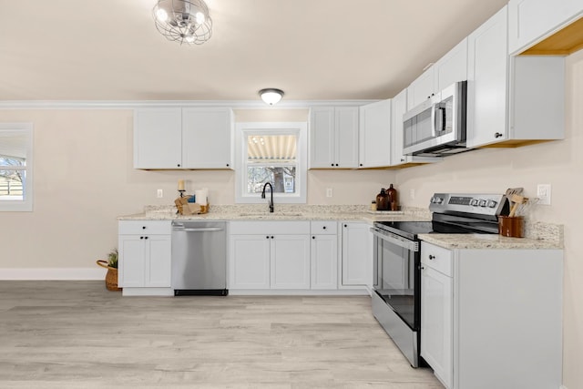 kitchen featuring white cabinets, light stone counters, stainless steel appliances, and a sink