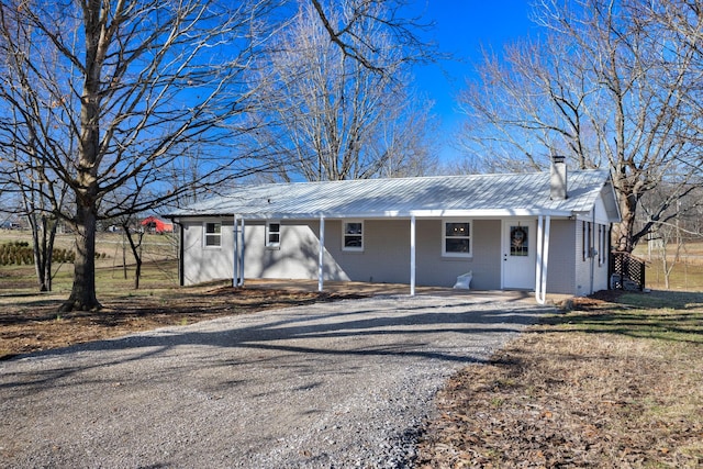 ranch-style house featuring metal roof, driveway, brick siding, and a chimney