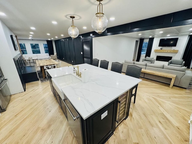 kitchen with a large island, light wood-type flooring, light stone countertops, pendant lighting, and sink