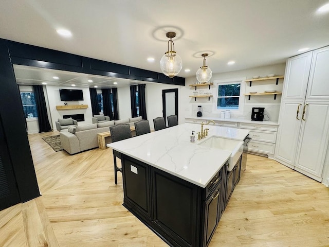 kitchen featuring white cabinetry, a center island with sink, light wood-type flooring, hanging light fixtures, and light stone countertops