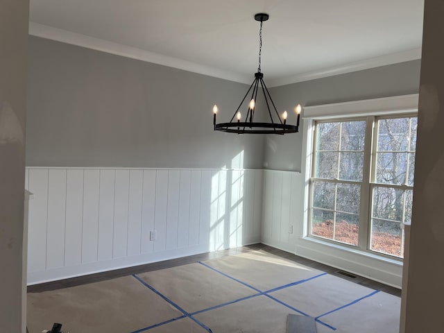 unfurnished dining area with crown molding, wainscoting, visible vents, and an inviting chandelier