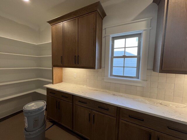 kitchen with tasteful backsplash, dark brown cabinetry, and light stone countertops