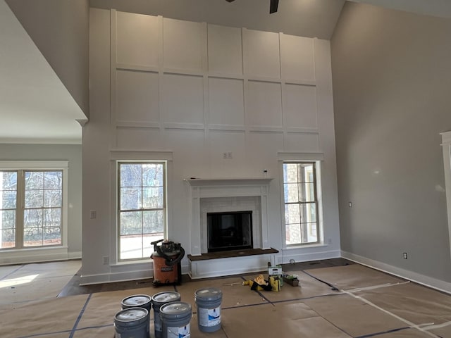 unfurnished living room featuring a ceiling fan, a glass covered fireplace, baseboards, and a high ceiling