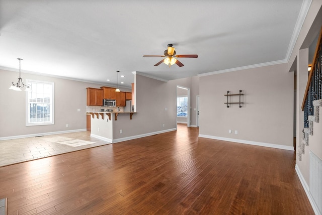 unfurnished living room featuring ornamental molding, dark hardwood / wood-style flooring, and ceiling fan with notable chandelier