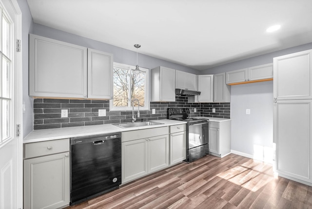 kitchen with light hardwood / wood-style floors, black appliances, pendant lighting, decorative backsplash, and sink