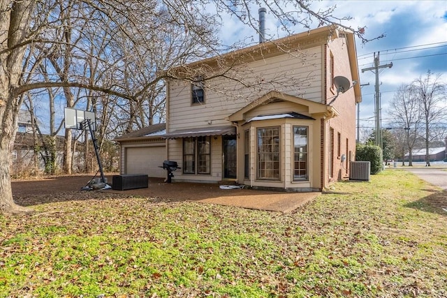 rear view of property with a garage, cooling unit, and a lawn