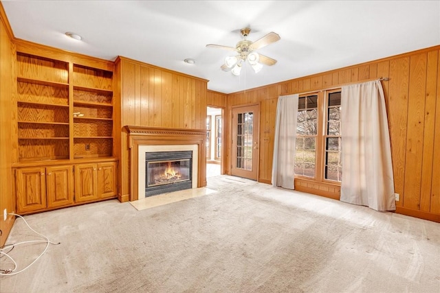 unfurnished living room with ceiling fan, built in features, light carpet, and wooden walls