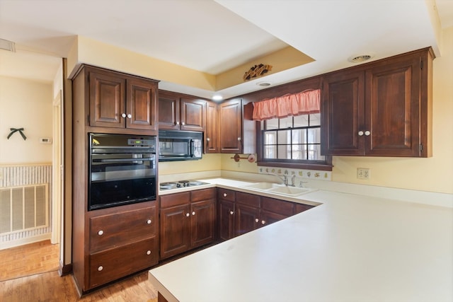 kitchen featuring sink, black appliances, light wood-type flooring, and kitchen peninsula