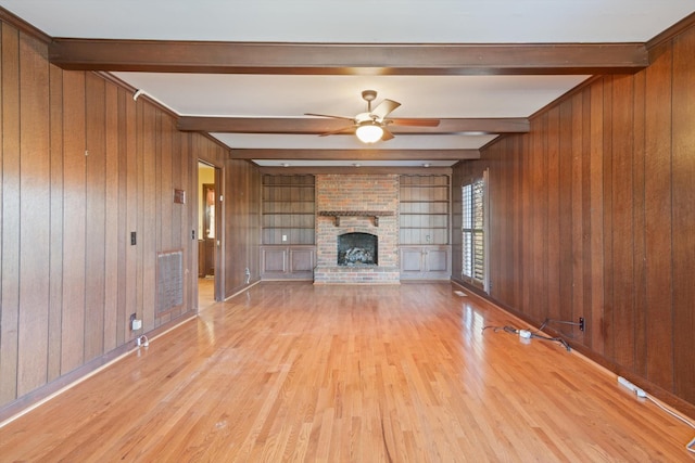 unfurnished living room with wood walls, beamed ceiling, and a brick fireplace