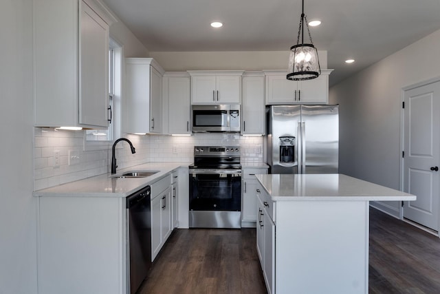 kitchen with decorative light fixtures, a kitchen island, sink, white cabinetry, and appliances with stainless steel finishes