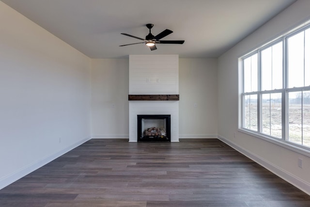 unfurnished living room featuring ceiling fan, dark wood-type flooring, a wealth of natural light, and a fireplace