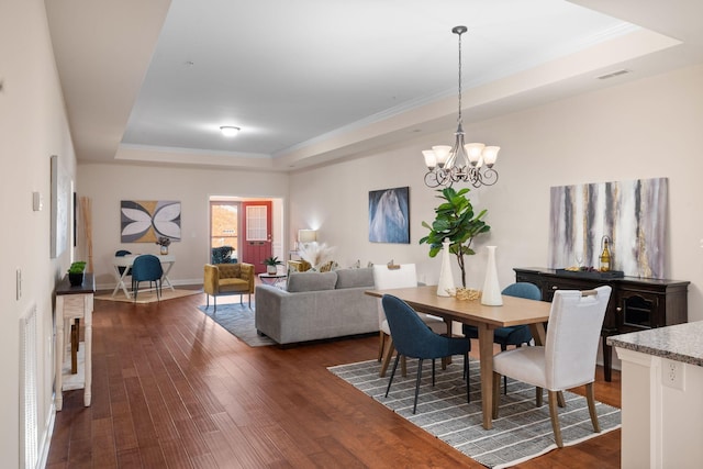 dining space featuring a chandelier, a raised ceiling, crown molding, and dark wood-type flooring