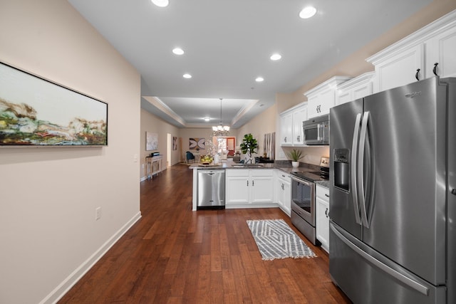 kitchen with kitchen peninsula, a raised ceiling, appliances with stainless steel finishes, white cabinetry, and an inviting chandelier