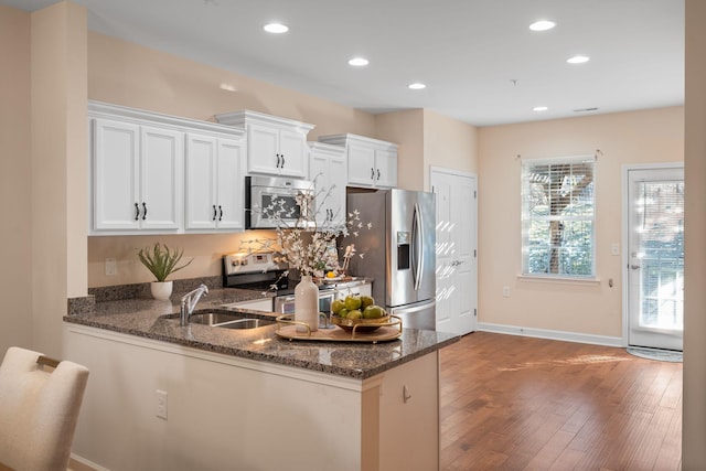 kitchen featuring appliances with stainless steel finishes, white cabinetry, dark hardwood / wood-style flooring, dark stone countertops, and kitchen peninsula