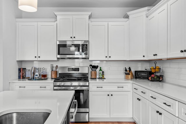 kitchen featuring backsplash, white cabinetry, appliances with stainless steel finishes, and light hardwood / wood-style flooring